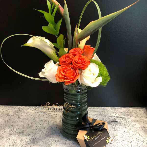 Orange and white roses in a tall glass vase with tropical leaves