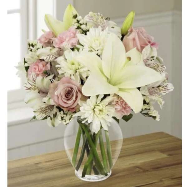 Bouquet of white lilies, pink roses, and white daisies in a clear glass vase