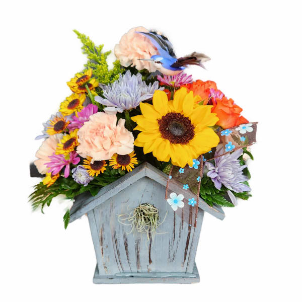 Mixed flower arrangement in a rustic birdhouse container with a ribbon