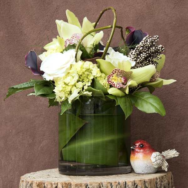 White and pale green floral arrangement in a glass vase with a small bird figurine
