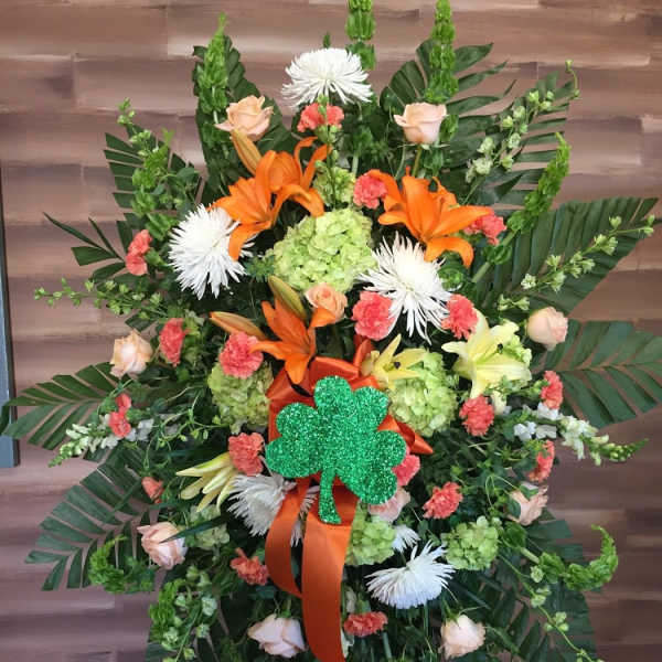 Large floral standing spray with orange lilies and a green shamrock accent