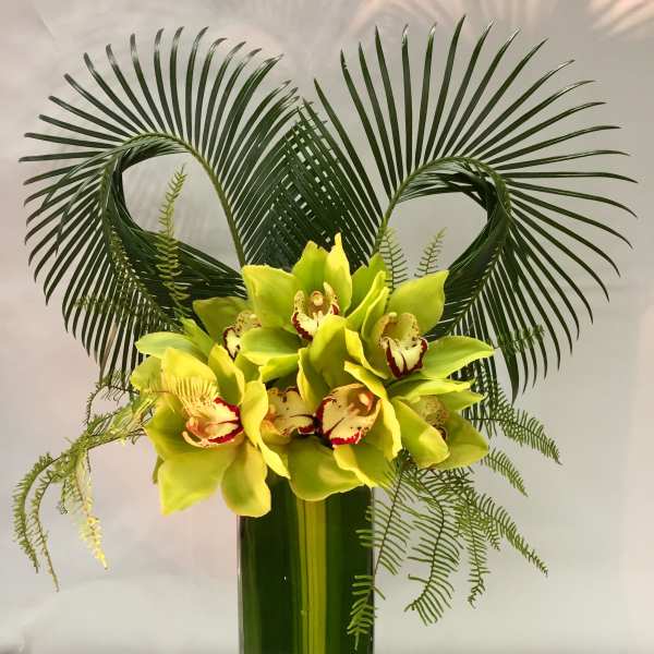 Green orchid arrangement in a tall glass vase with palm fronds
