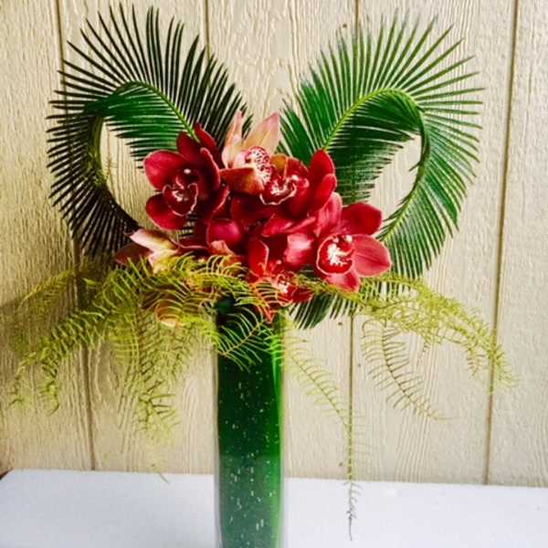 Red orchid arrangement in a tall green vase with palm fronds