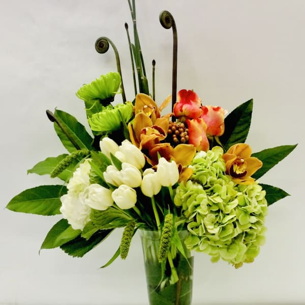 Mixed floral arrangement in a glass vase with green hydrangea and orchids