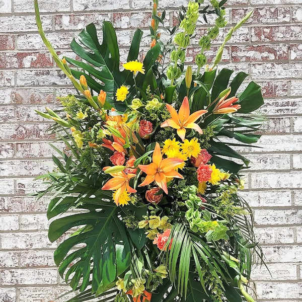 Tall tropical floral spray with orange lilies and yellow blooms on a stand