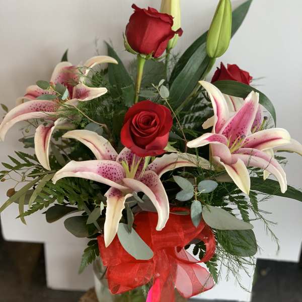 Arrangement of red roses and pink lilies in a clear glass vase with a red bow.