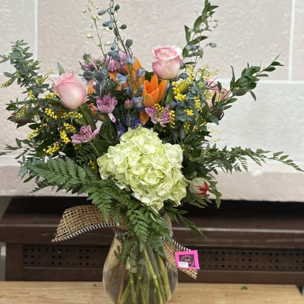Mixed bouquet in a glass vase with pink roses and a green hydrangea bloom