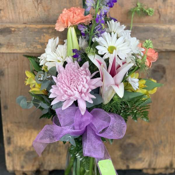 Mixed bouquet with pink, white, purple, and yellow flowers in a glass vase