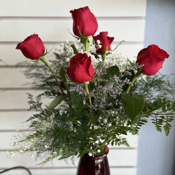 Red roses arranged in a burgundy vase with airy filler flowers