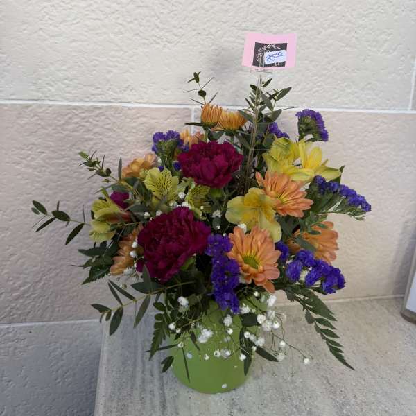 Mixed bouquet in a green container with orange, yellow, purple, and magenta flowers