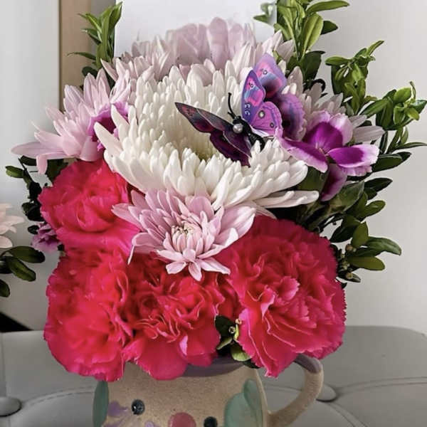 Pink and white flowers arranged in a painted ceramic mug with butterfly decorations.