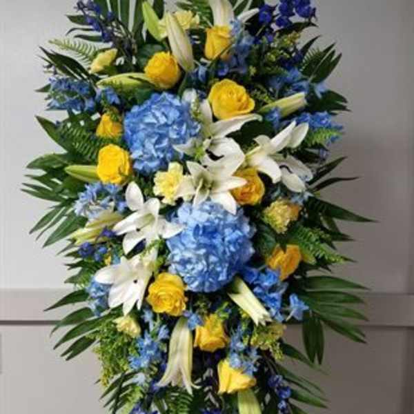 Tall blue, yellow, and white funeral spray on a stand