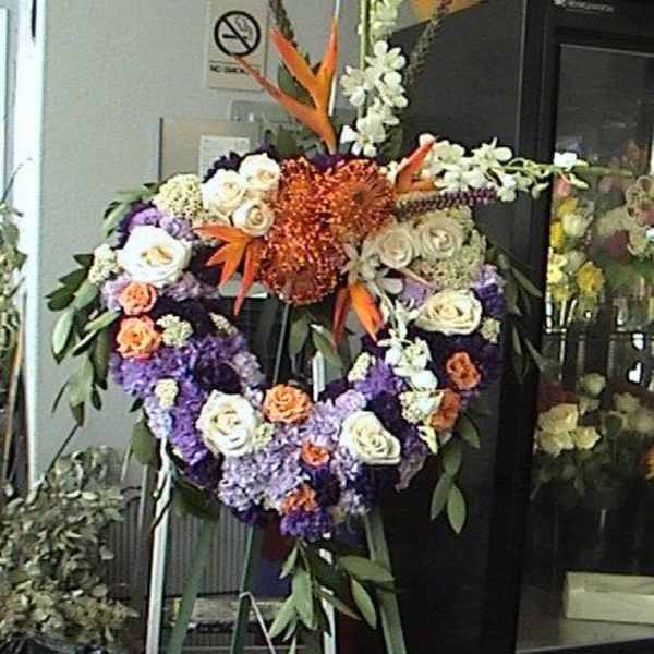 Heart-shaped floral wreath with white, purple, and orange flowers on an easel