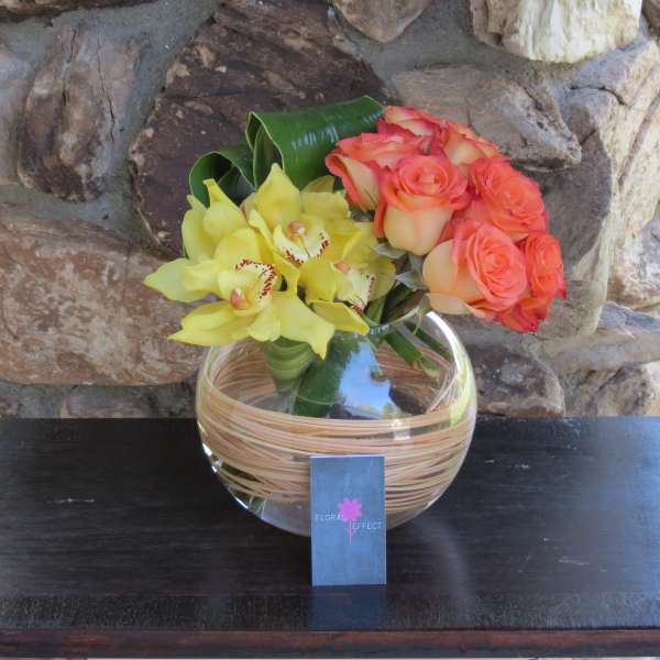 Bouquet of orange roses and yellow orchids in a round glass vase