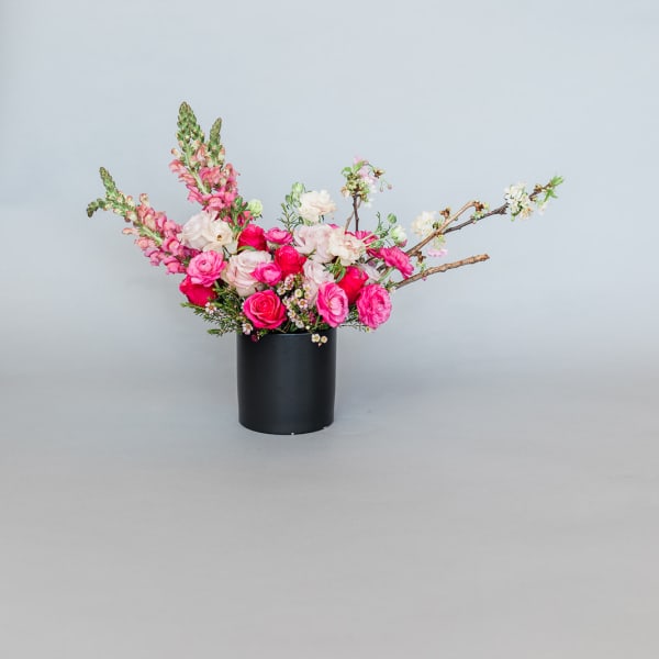 Pink and white floral arrangement in a black cylindrical vase