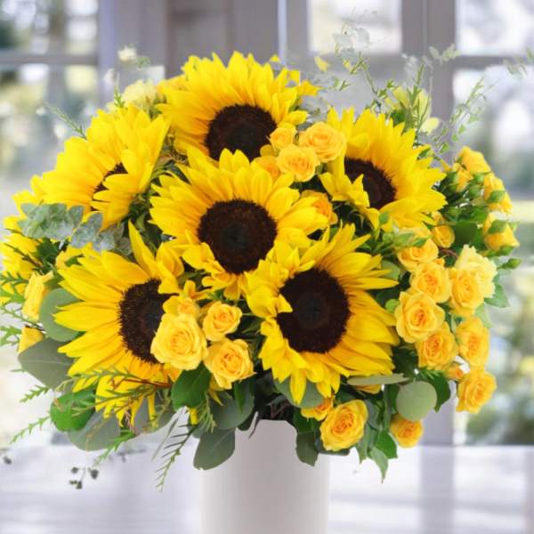 Bouquet of yellow sunflowers and small yellow roses in a white vase