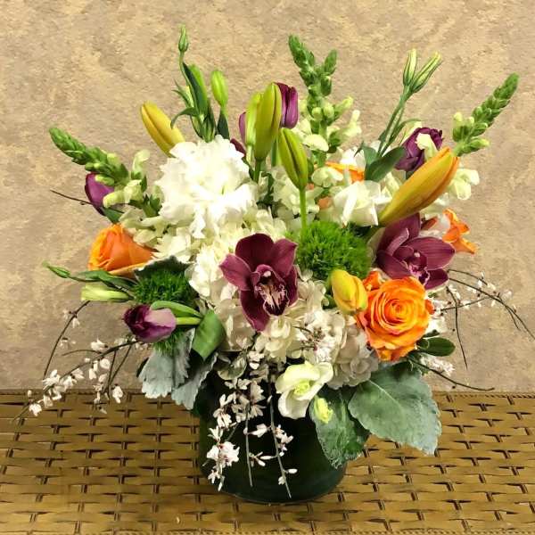 Mixed bouquet with orange roses, purple orchids, white blooms, and lilies in a vase