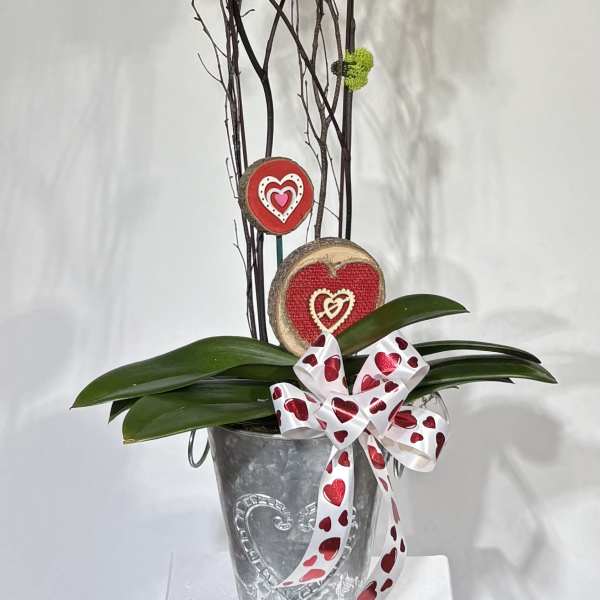 Pink orchids in a metal vase with heart decorations and a ribbon