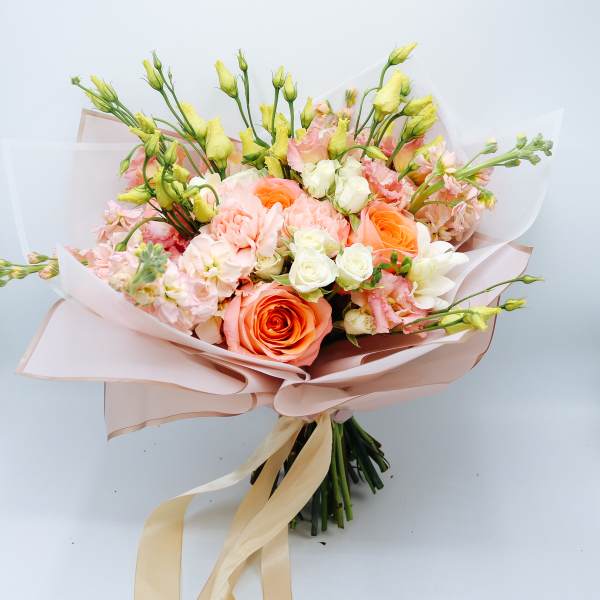 Bouquet of peach and white roses with pale pink blooms wrapped in blush paper
