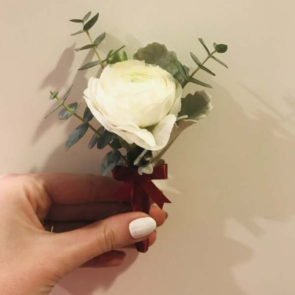 Small white flower boutonniere with greenery and a burgundy ribbon