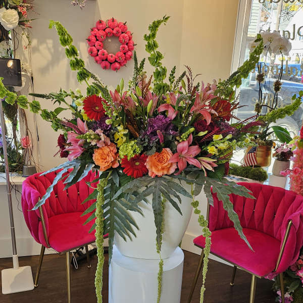 Large mixed flower arrangement in a white pedestal vase with pink and orange blooms