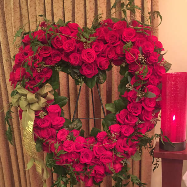Heart-shaped wreath of red roses with a ribbon on a stand