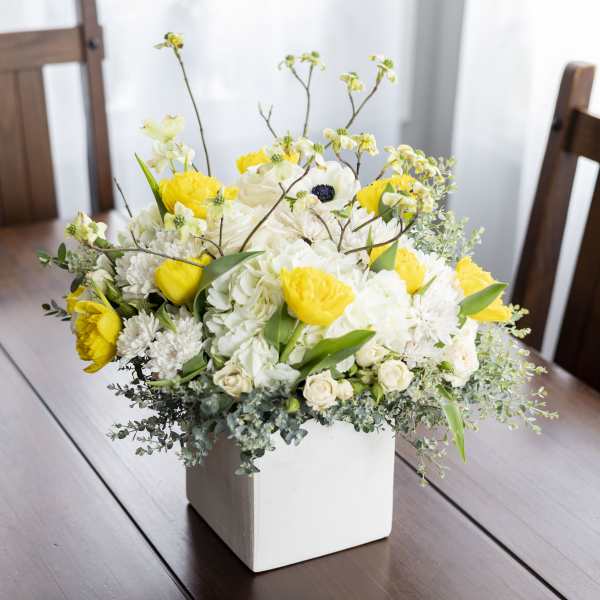 Yellow and white floral arrangement in a white square vase