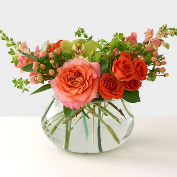 Pink and orange roses arranged in a clear glass vase