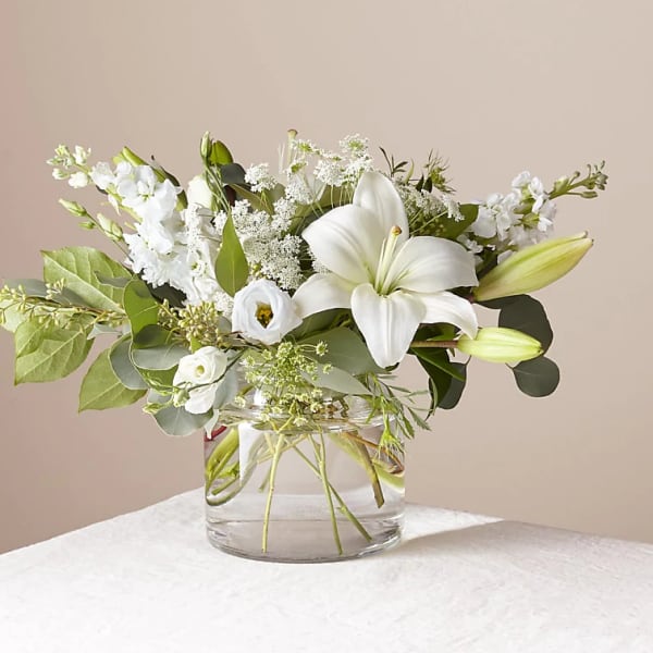 White lilies and mixed white flowers in a clear glass vase