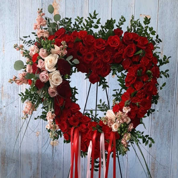 Heart-shaped red rose wreath on a stand with pink accents and ribbon tails