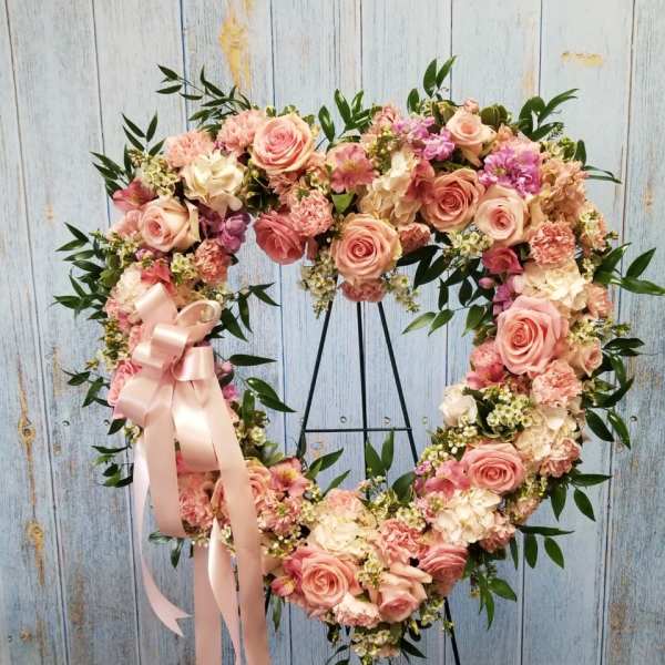 Heart-shaped floral wreath with pink roses and a satin ribbon on a stand