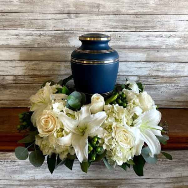 White floral urn arrangement with lilies and roses around a blue urn