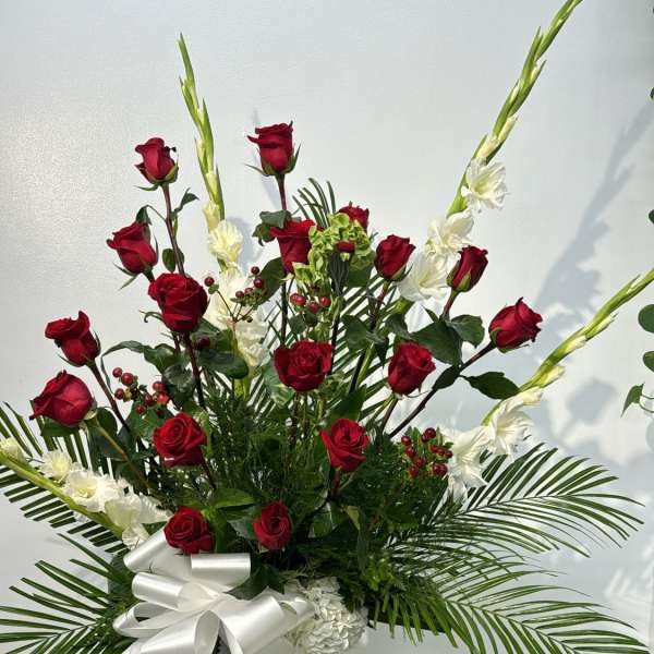 Tall floral arrangement with red roses and white flowers in a wicker pedestal vase
