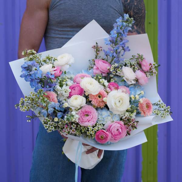 Large bouquet of pink, white, and blue flowers wrapped in white paper