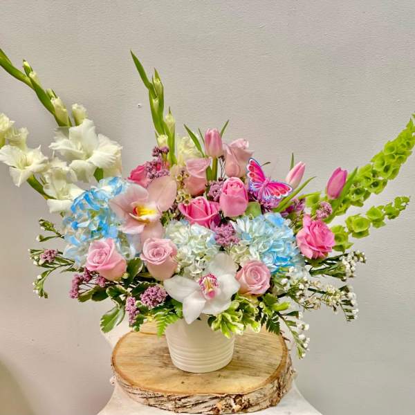 Mixed bouquet of pink roses, orchids, and blue hydrangeas in a white vase