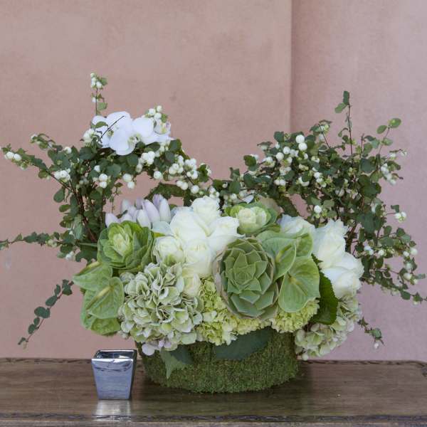 White and green floral arrangement in a moss-covered container