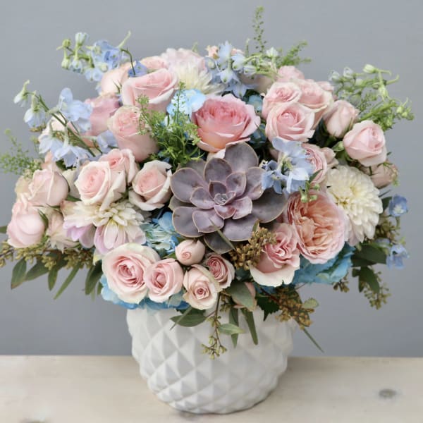 Pink roses and blue flowers arranged in a white textured vase