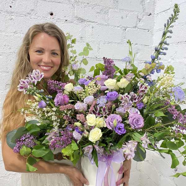 Woman holding a large lavender and white floral arrangement in a white box