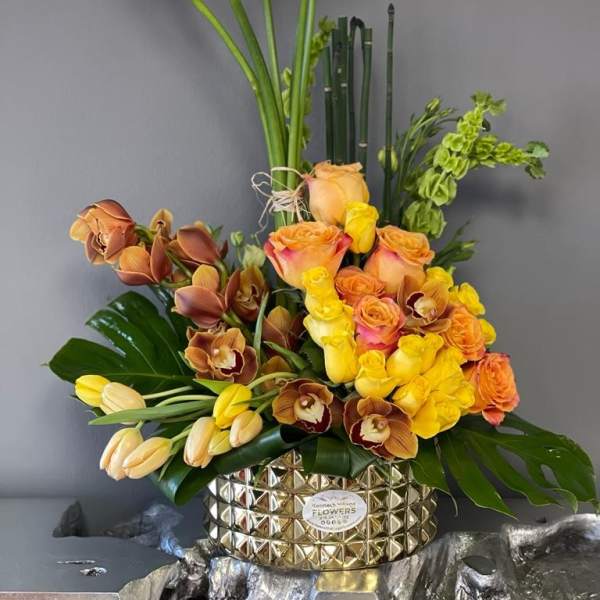 Tall floral arrangement with white calla lilies, roses, and orchids in a gold vase