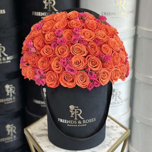 Round bouquet of orange and pink roses in a black hat box