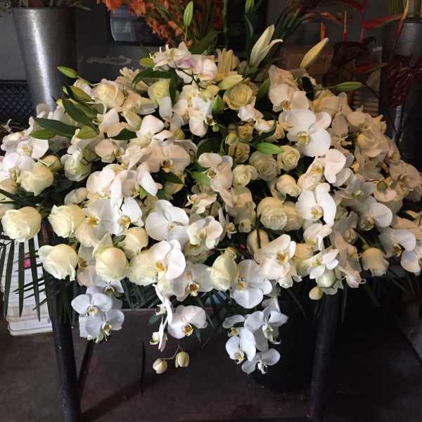 Large white orchid and rose arrangement in a black container