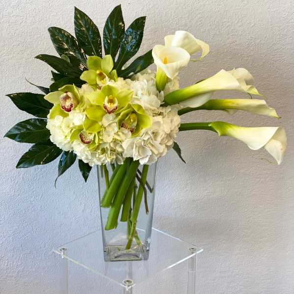 White calla lilies and green orchids in a clear glass vase