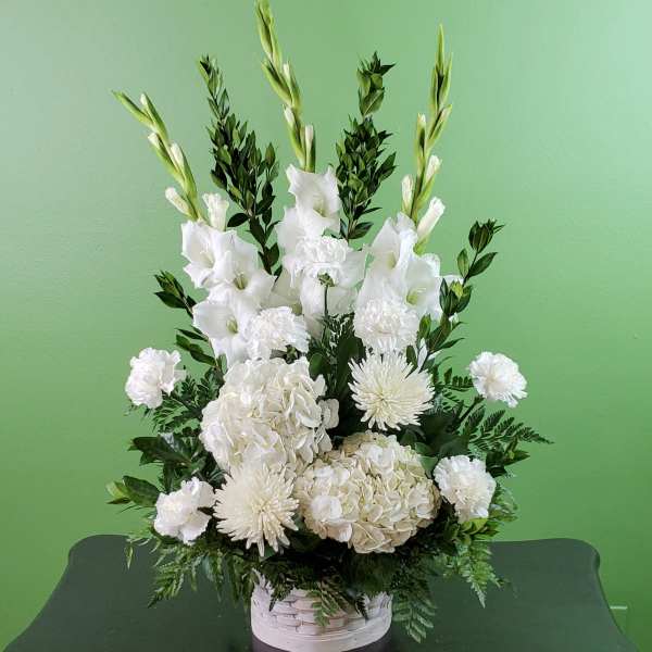 White floral arrangement in a white basket with tall gladiolus and hydrangeas