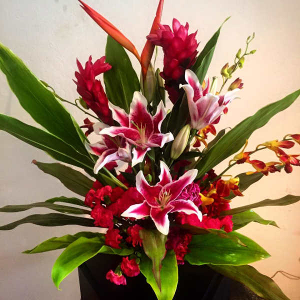 Tropical bouquet with pink lilies and red orchids in a black container