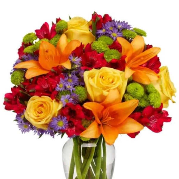 Colorful bouquet of roses, lilies, and daisies in a clear glass vase