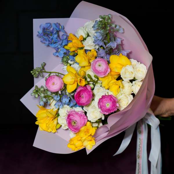 Bouquet of yellow, pink, white, and blue flowers wrapped in pink paper