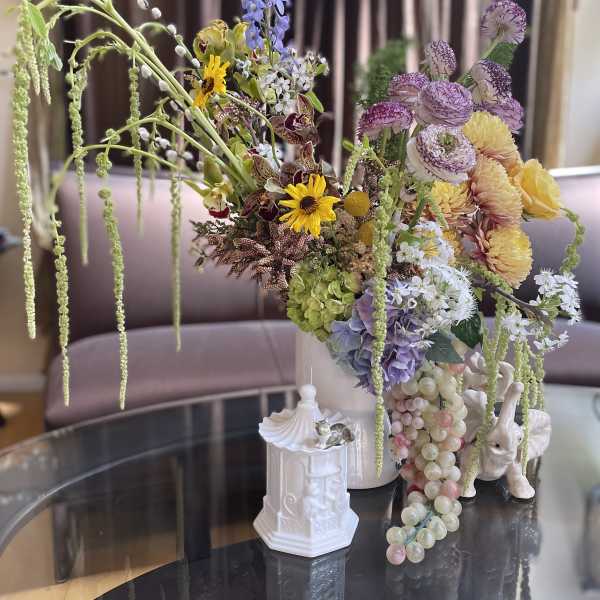 Large mixed floral arrangement in a white vase with cascading blooms