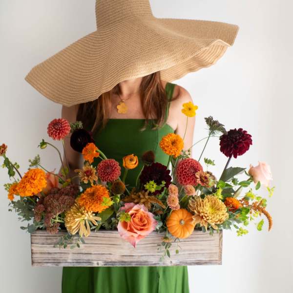 Woman in a green dress holding a wooden box of colorful flowers