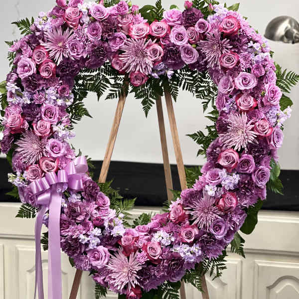 Heart-shaped pink and purple floral wreath on an easel with a ribbon bow