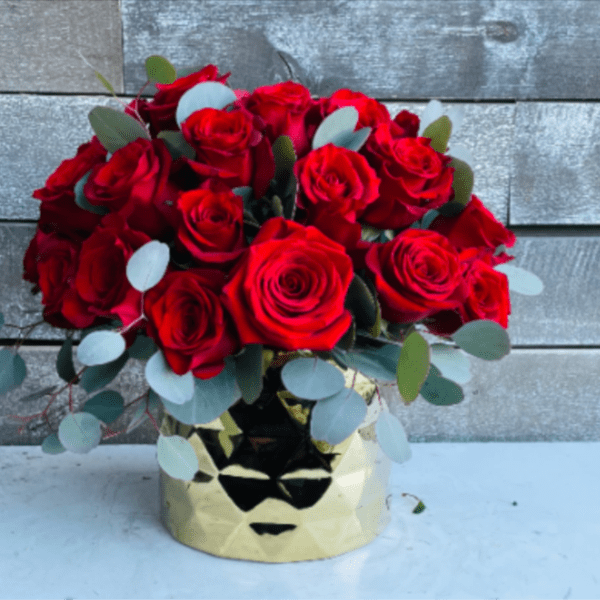 Red roses arranged in a gold vase with eucalyptus accents